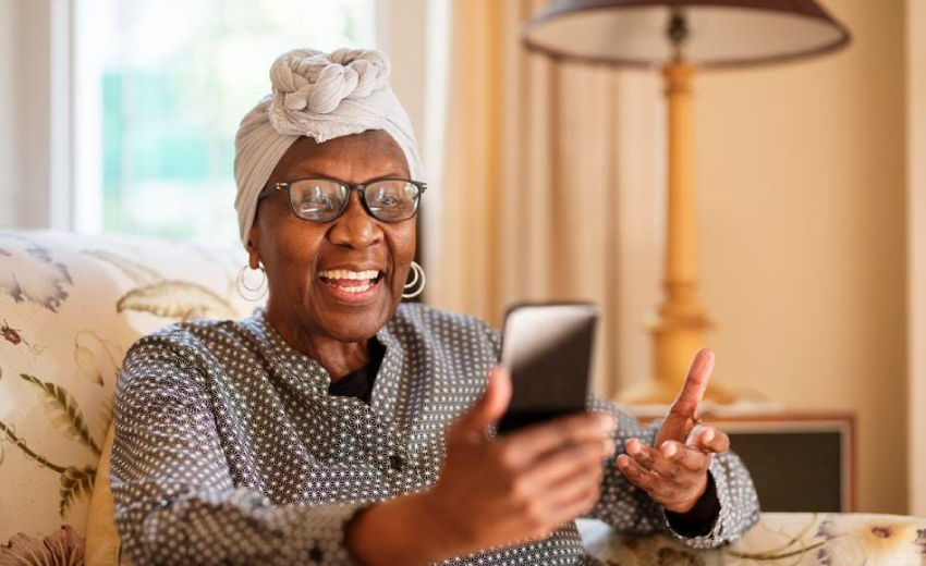 An elderly woman with a wide smile using her phone for communication