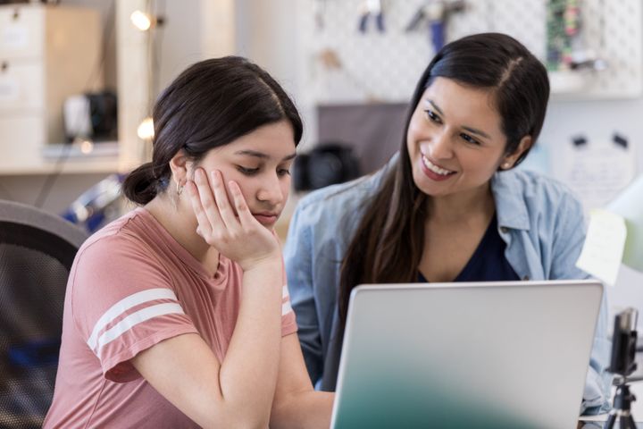 A woman advising a young girl with an open laptop in front of them.