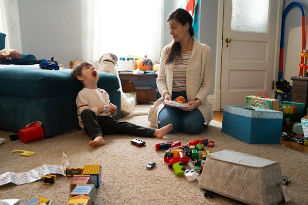 A Mother looking at her son while he is yawning with toys all around